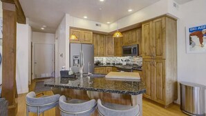 A modern kitchen with granite countertops, wooden cabinets, and a central island with bar stools.