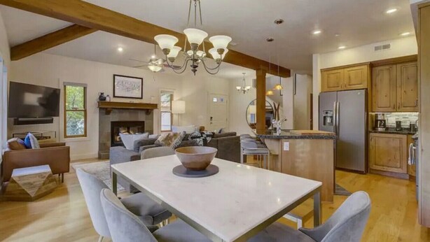 A spacious living area with a dining table, grey upholstered chairs, a fireplace, a sofa set, and wooden beams on the ceiling.