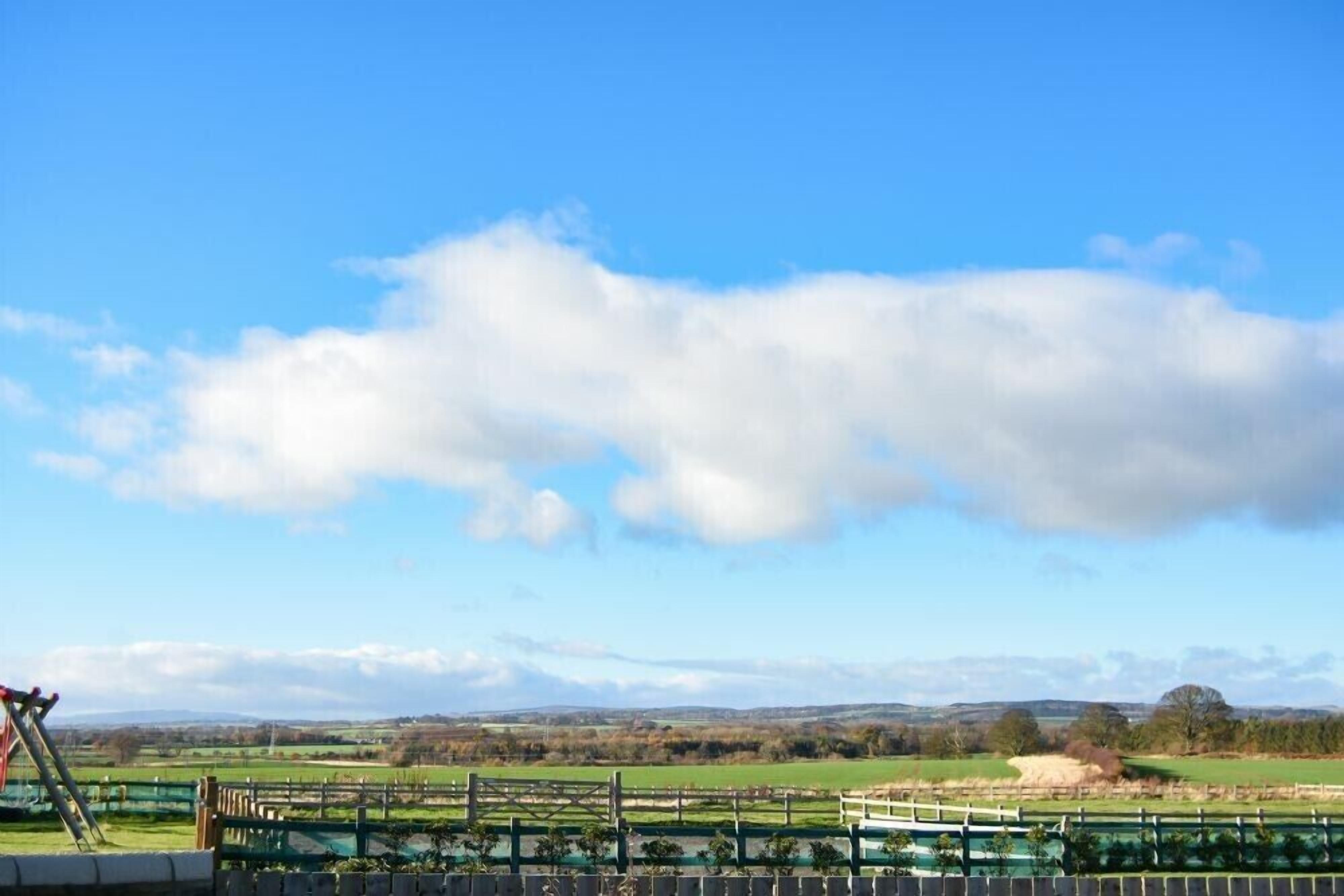 A rural landscape with a clear sky, a wooden fence, and distant fields.