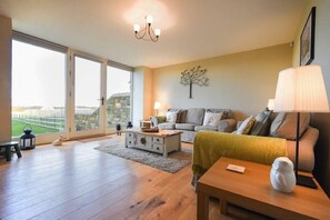 A spacious living room with a large window, a sofa set, a coffee table, and a lamp. - The Pepper Pot (Morpeth)