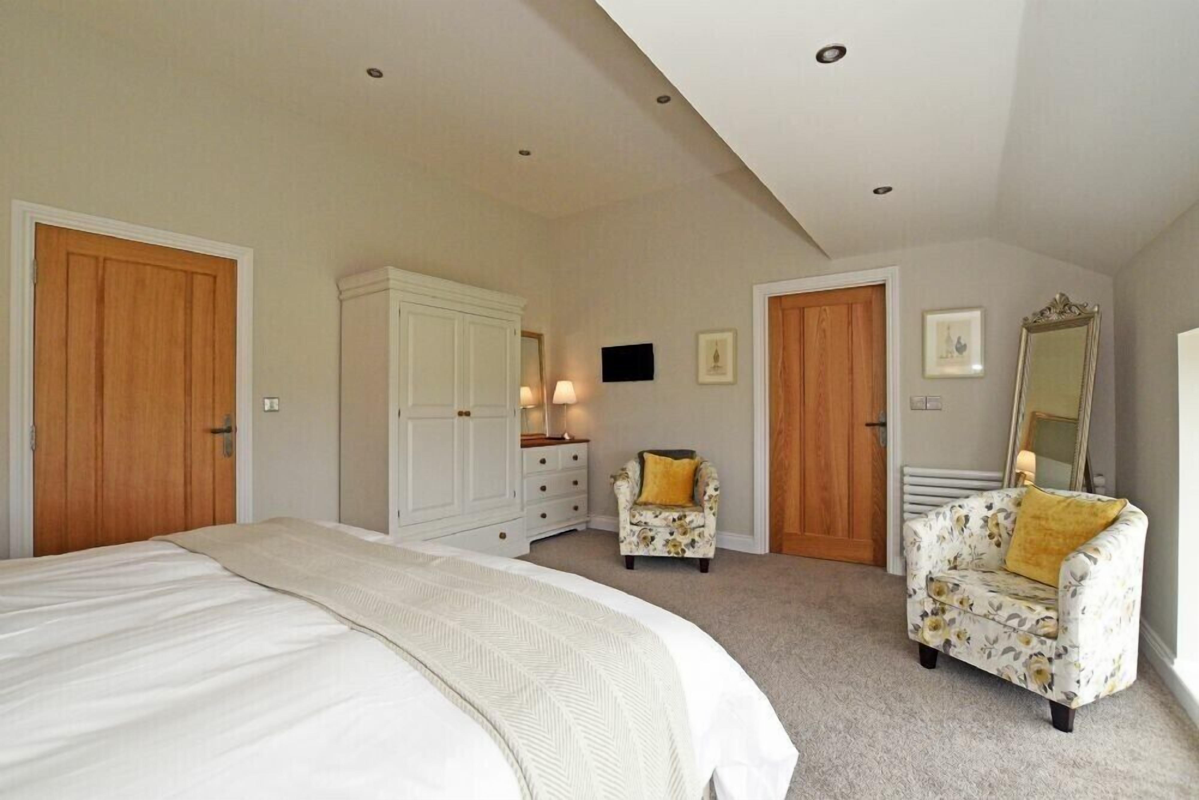 A bedroom with a large bed, two chairs, a dresser, and a mirror.
