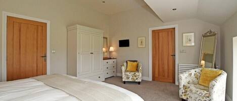 A bedroom with a large bed, two chairs, a dresser, and a mirror.