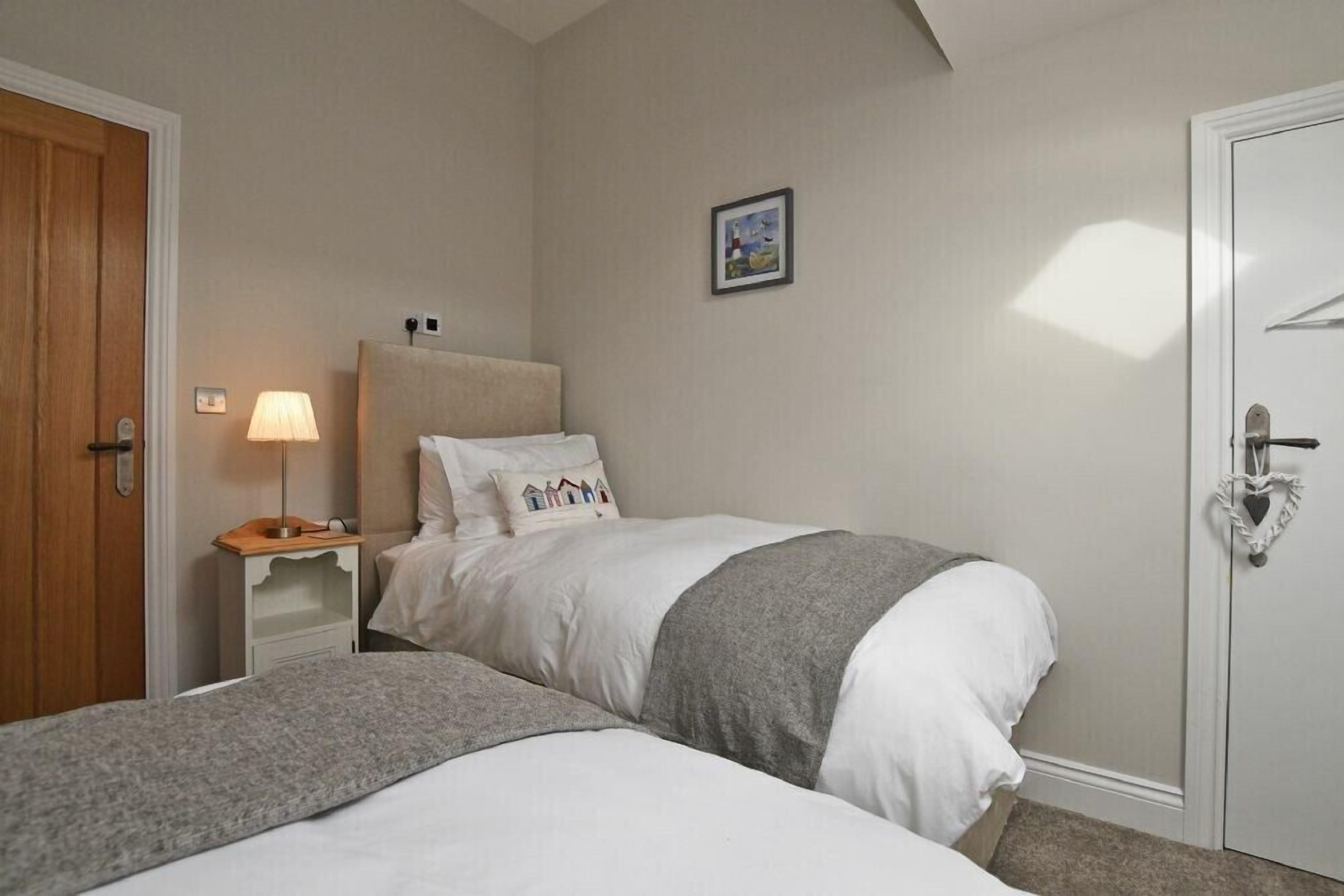 A bedroom with two beds, a bedside table with a lamp, a framed picture on the wall, and a door with a heart-shaped handle.