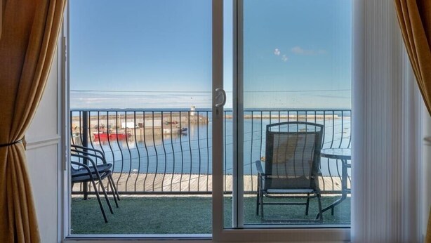 Uma varanda com vista para a praia, uma cadeira e uma mesa.