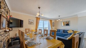 Uma sala de jantar com uma mesa posta para quatro pessoas, um sofá e uma televisão na parede.