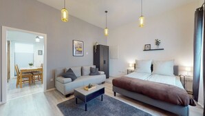 Ein modernes Schlafzimmer mit einem großen Bett, einer Couch, einem Couchtisch und einem Schreibtisch. Drei Pendelleuchten und ein Kleiderschrank sind vorhanden.