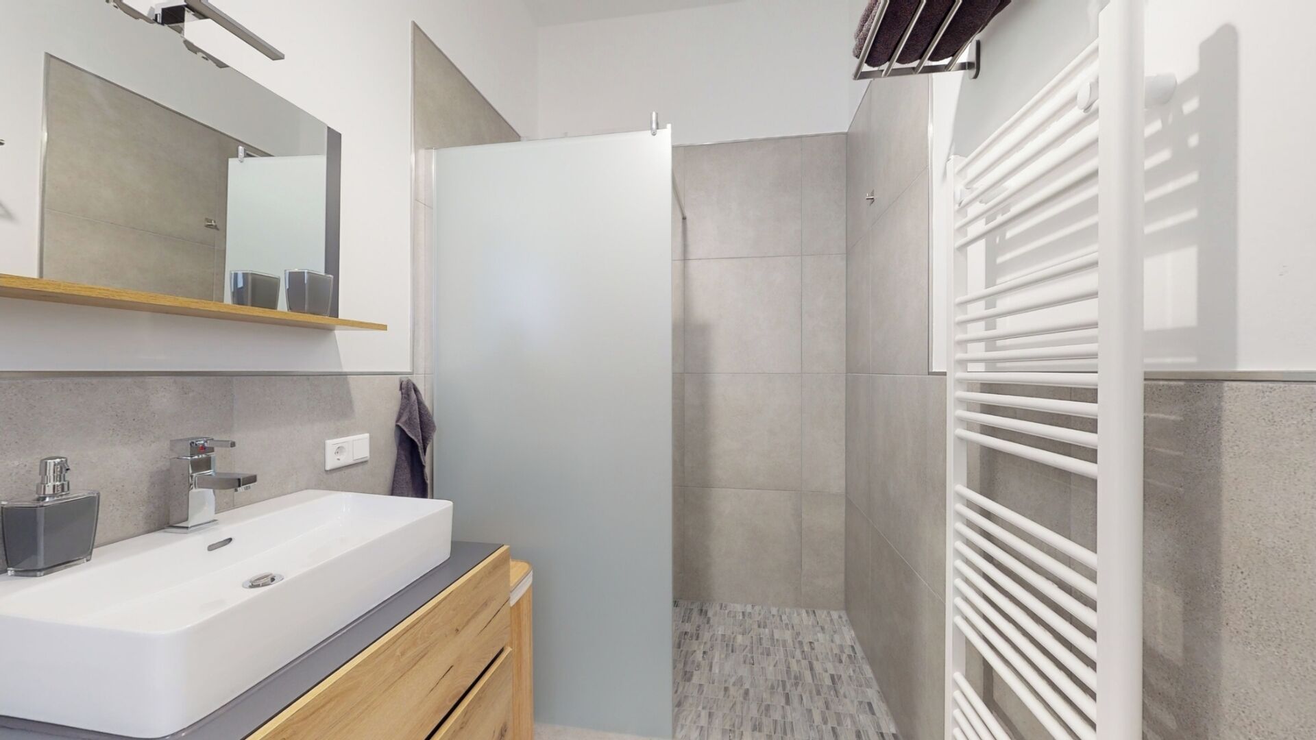 A modern bathroom with a large white sink, a mirror, and a shower area with a white towel rack.