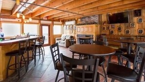 Un grand espace dédié à la salle à manger, avec des tables et des chaises en bois, un coin bar et un téléviseur fixé au mur.