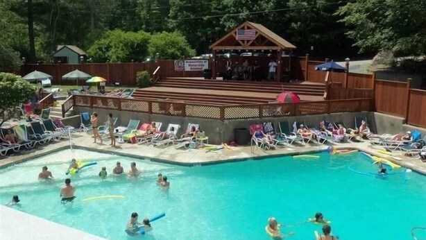 Un espace piscine comprenant plusieurs bassins, des chaises longues et une scène couverte ornée d’un drapeau américain.