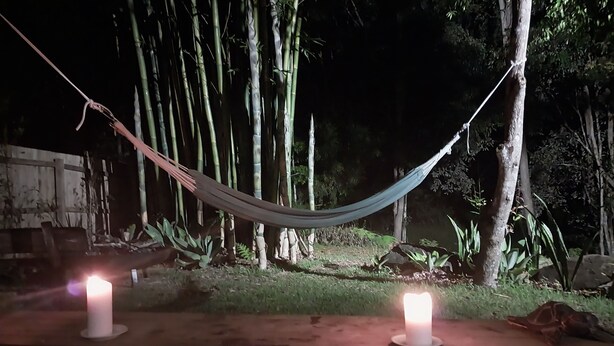 Una hamaca colgada entre árboles, con dos velas encendidas sobre una plataforma de madera.