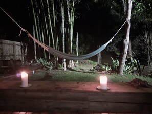 Una hamaca colgada entre árboles, con dos velas encendidas sobre una plataforma de madera.