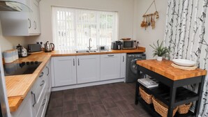 A compact kitchen with white cabinets, a wooden countertop, a washing machine, and a small table with baskets. - Rosedale Lodge (Alnwick)
