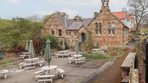 A stone building with a traditional architectural style, featuring a clock tower and a sign for 'The Old School Gallery'. - Rosedale Lodge (Alnwick)
