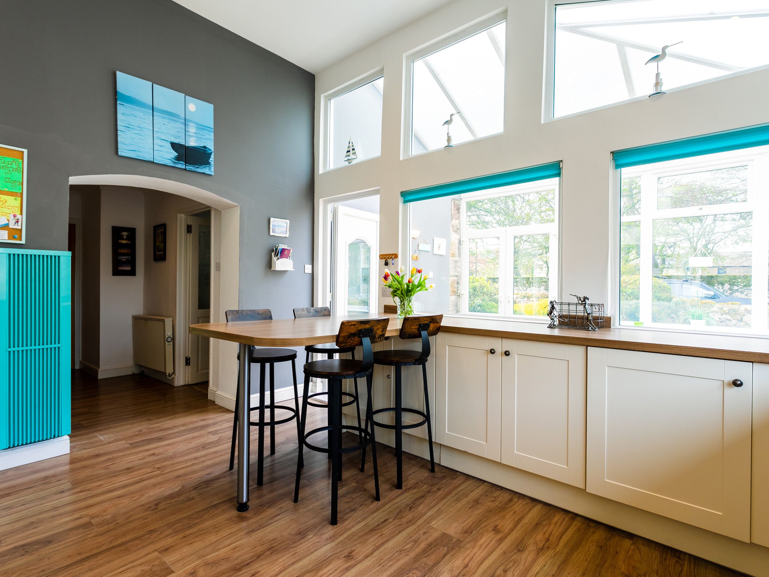 Una cocina moderna con una mesa de madera, taburetes de bar y ventanas amplias.