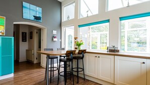 Una cocina moderna con una mesa de madera, taburetes de bar y ventanas amplias.