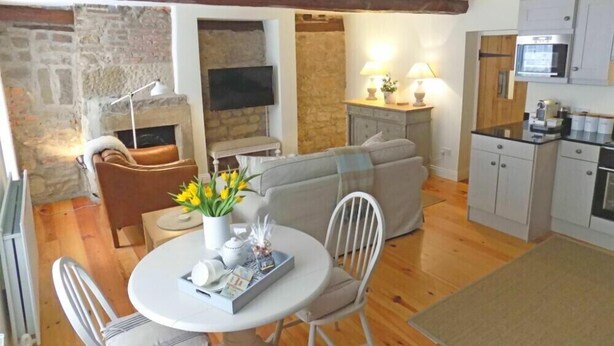 Ein gemütliches Wohnzimmer mit Kamin, einer Couch, einem Esstisch mit Blumenvase sowie einer Küchenzeile mit Schränken und einer Mikrowelle.