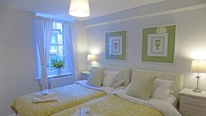 Ein Hotelzimmer mit zwei Betten, einem Fenster mit Vorhängen und gerahmten Bildern an der Wand.