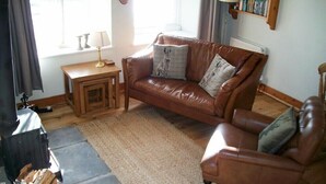 A cozy living room with a leather sofa, a small wooden side table, and a rug. - Swallow Cottage (Alnwick)