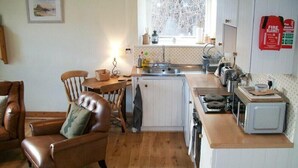 A compact kitchen with a wooden countertop, a small stove, a microwave, and a window with a view of trees. - Swallow Cottage (Alnwick)