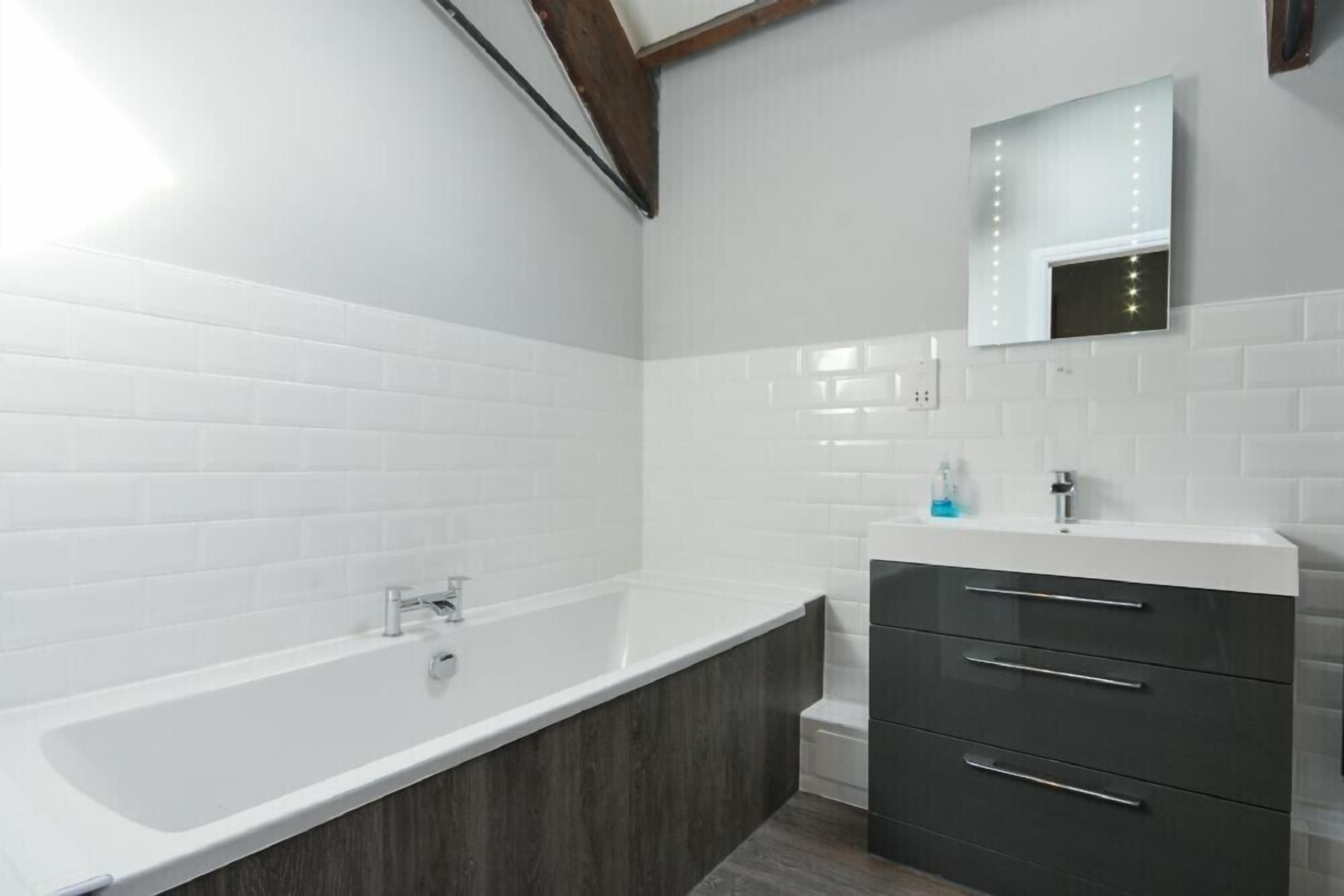 Un bagno moderno con una vasca freestanding, un mobile vanitario con specchio e piastrelle bianche tipo metro.