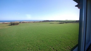 Vista desde una ventana sobre un campo verde y un horizonte lejano.
