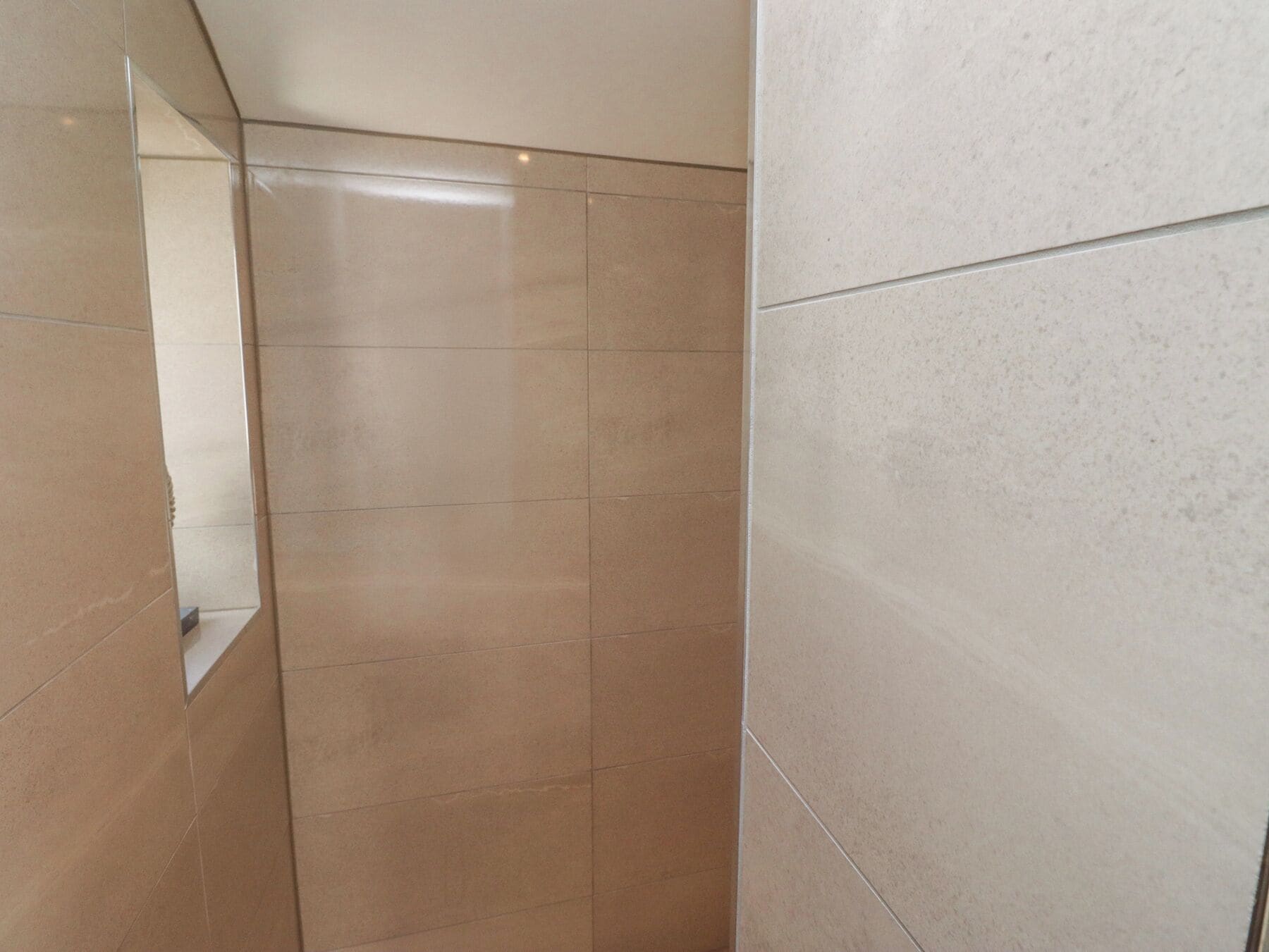 A tiled shower area with a mirror on the left.