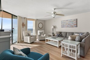 Un salón espacioso con balcón, ventilador de techo, sofá, mesa de centro y vista al océano.
