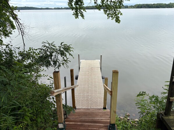 A wooden dock leading into a calm lake, surrounded by greenery. - A Lakeside Log Cabin Built in 1858 (Grove City)