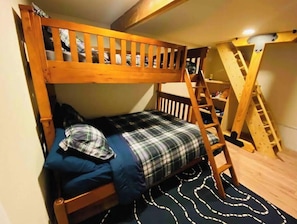 Een stapelbed met een ladder, een geruit beddeken en een donker, patroonrijk vloerkleed.