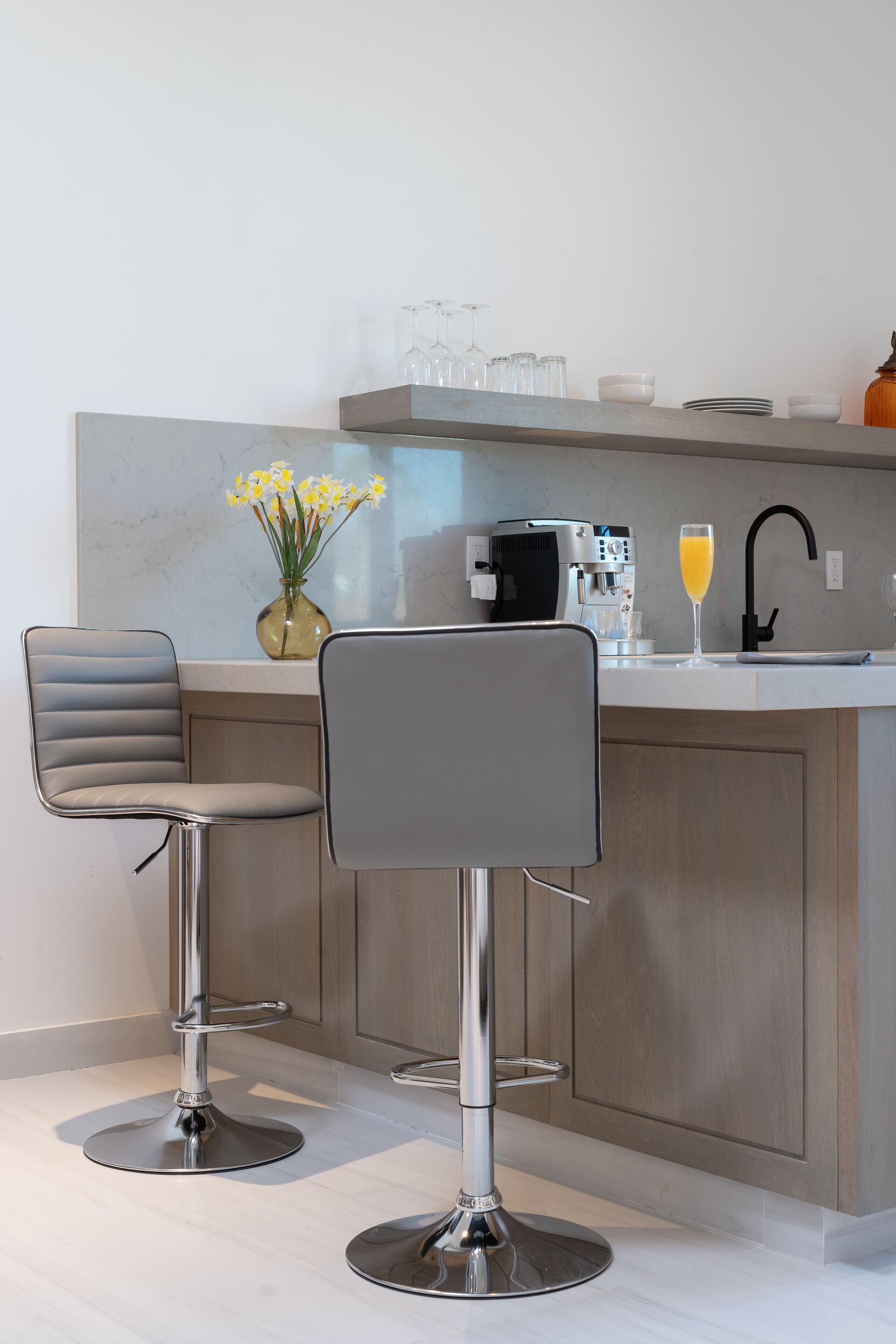 A modern kitchen with two bar stools, a coffee machine, and a glass of orange juice on the counter.