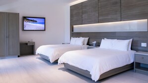 A modern bedroom with two beds, a TV on the wall, and a wooden headboard. - Aventuras Hotel (Loreto)