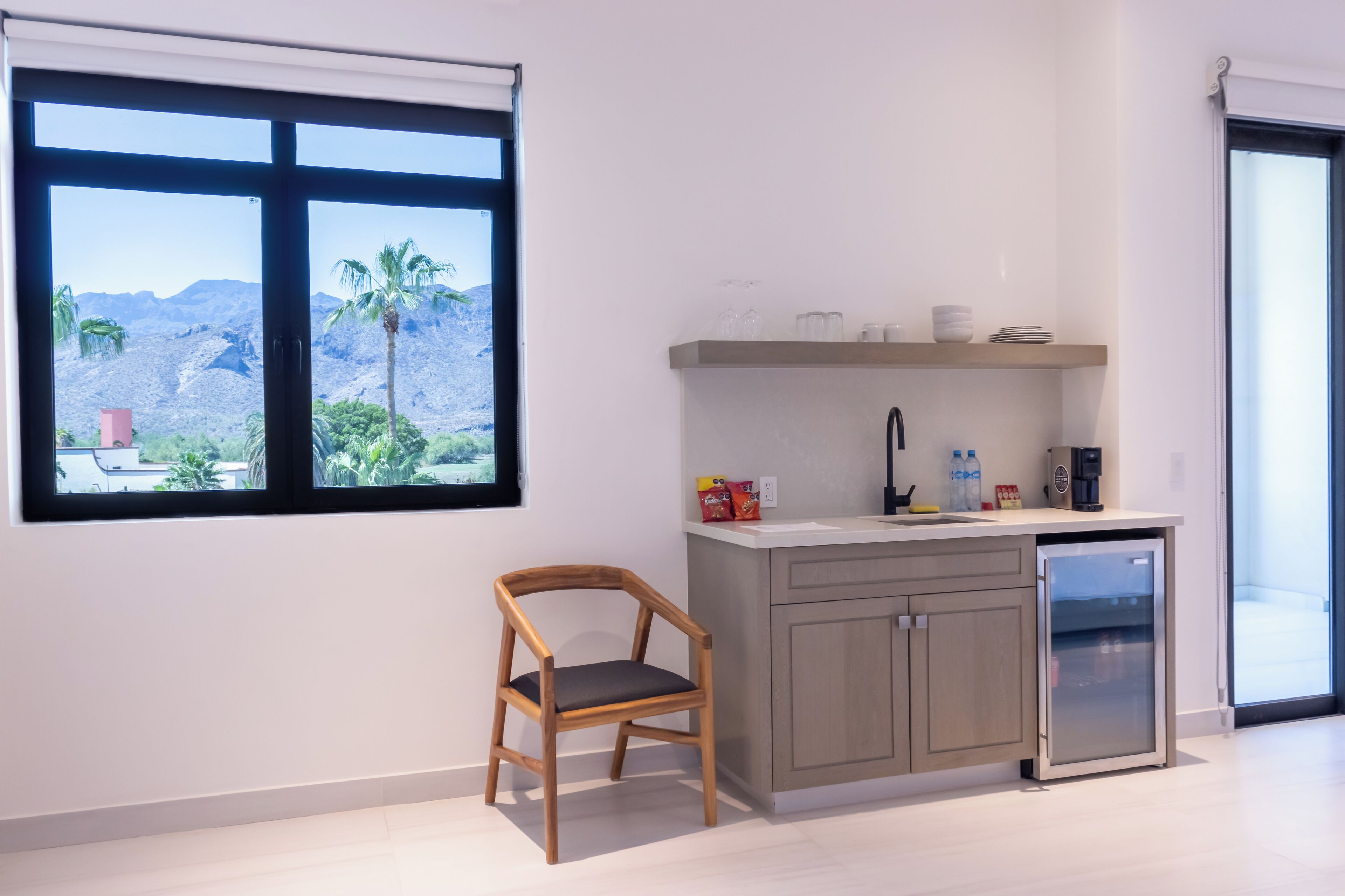 Cocina moderna con vistas a palmeras y montañas, una silla de madera y un refrigerador pequeño.