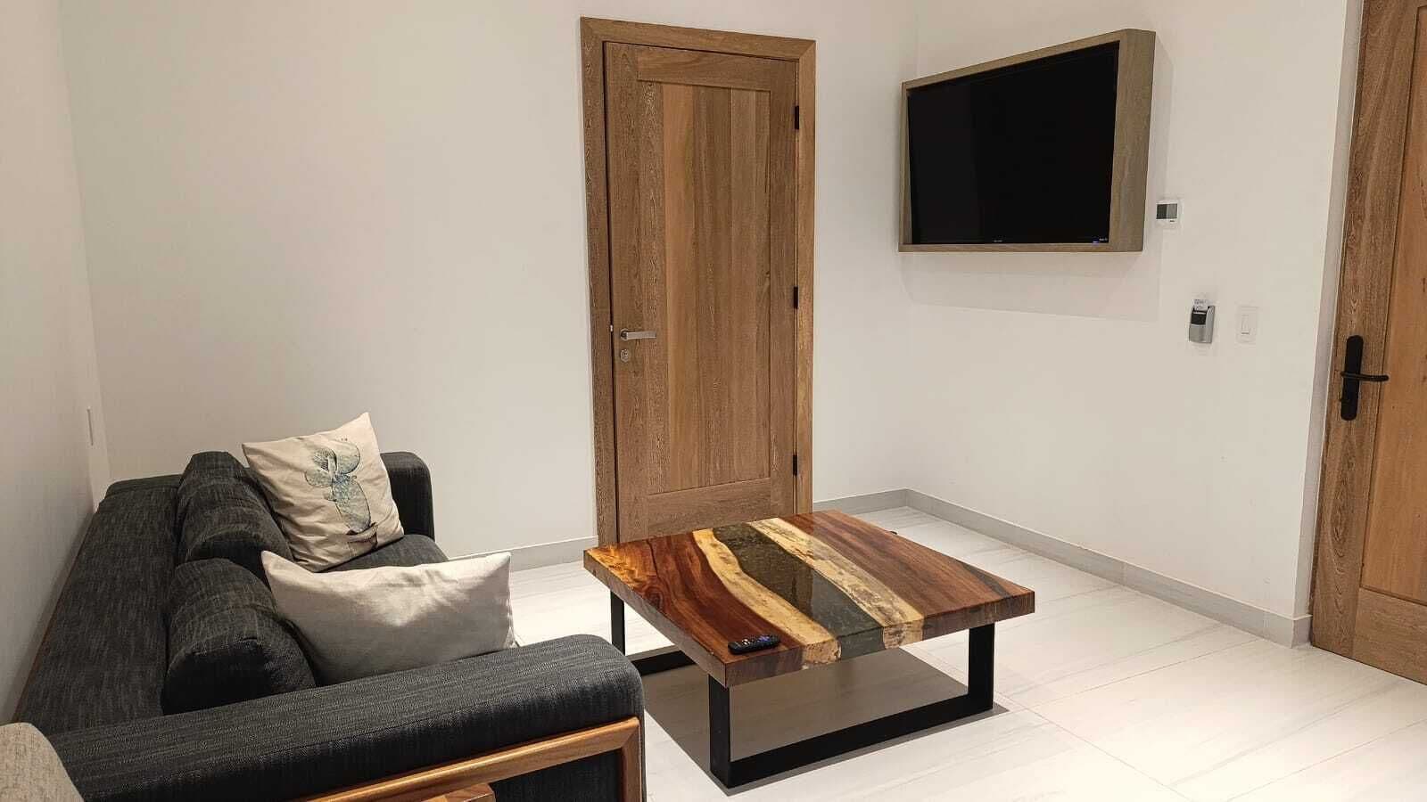 A living room with a sofa, a coffee table with a wood grain design, a wooden door, and a mounted TV.