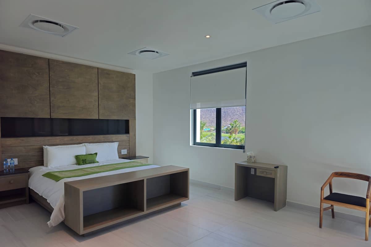 Quarto moderno com cama, mesas de cabeceira, espaço para objetos pessoais junto à cama e armários embutidos. Janela com vista.