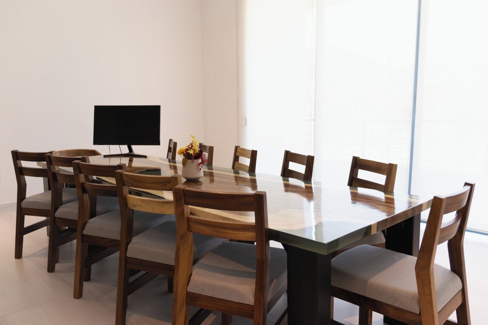 A conference room with a large glass table, wooden chairs, a flat-screen TV, and a vase with flowers.
