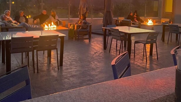 An outdoor seating area with tables and chairs, a fire pit, and a view of mountains during sunset. - Aventuras Hotel (Loreto)