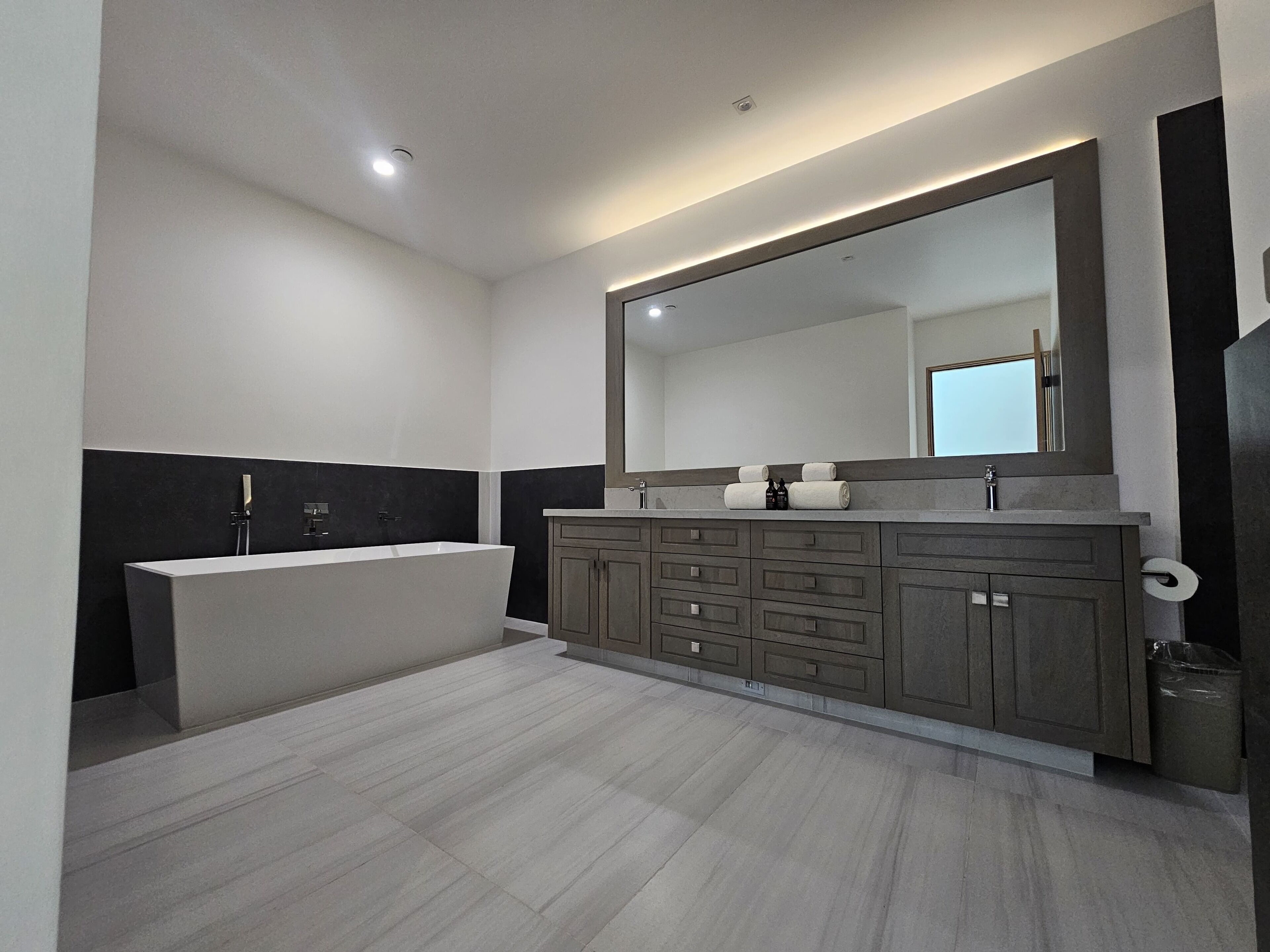 A modern bathroom with a large mirror, a bathtub, and a vanity with multiple drawers.