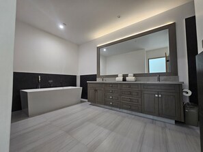 Ein modernes Badezimmer mit einem großen Spiegel, einer Badewanne und einem Schminktisch mit mehreren Schubladen.