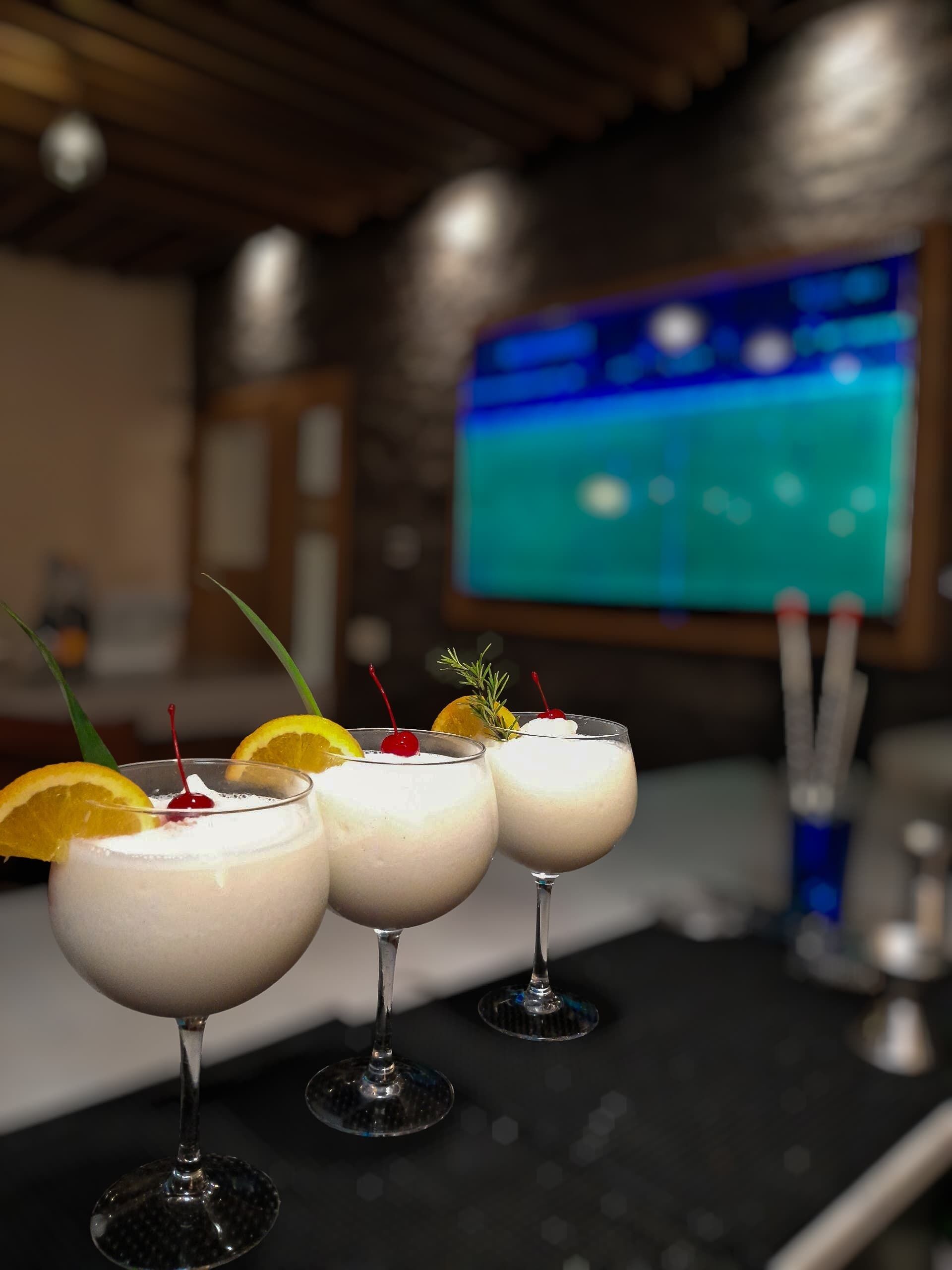 Three cocktails with garnishes on a bar counter.