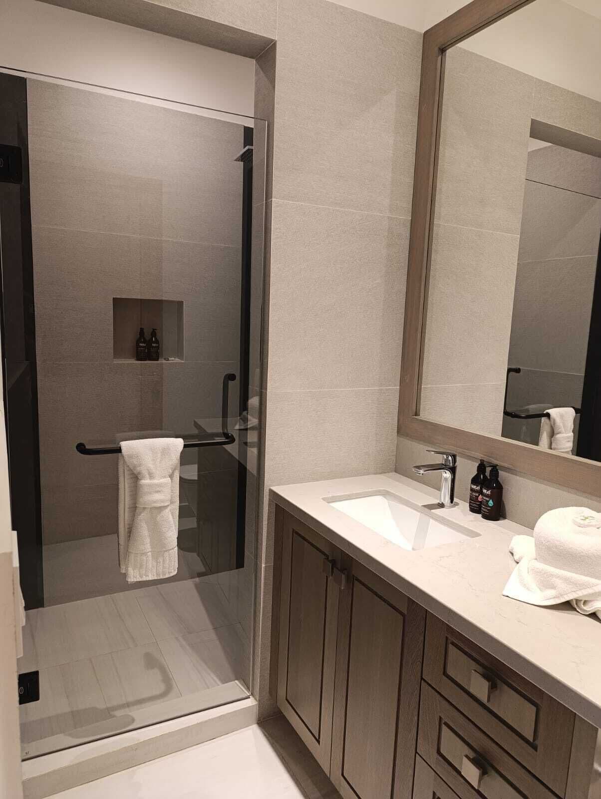 A modern bathroom with a glass shower enclosure, a large mirror, and a vanity with a sink and storage cabinets.