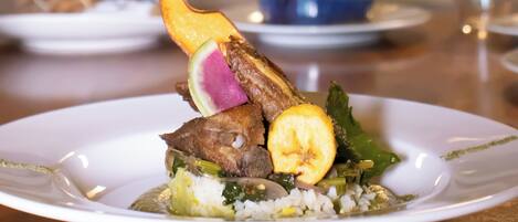 Un plato emplatado con pato como pieza central, adornado con una rodaja de naranja y un elemento morado, sobre un plato blanco.