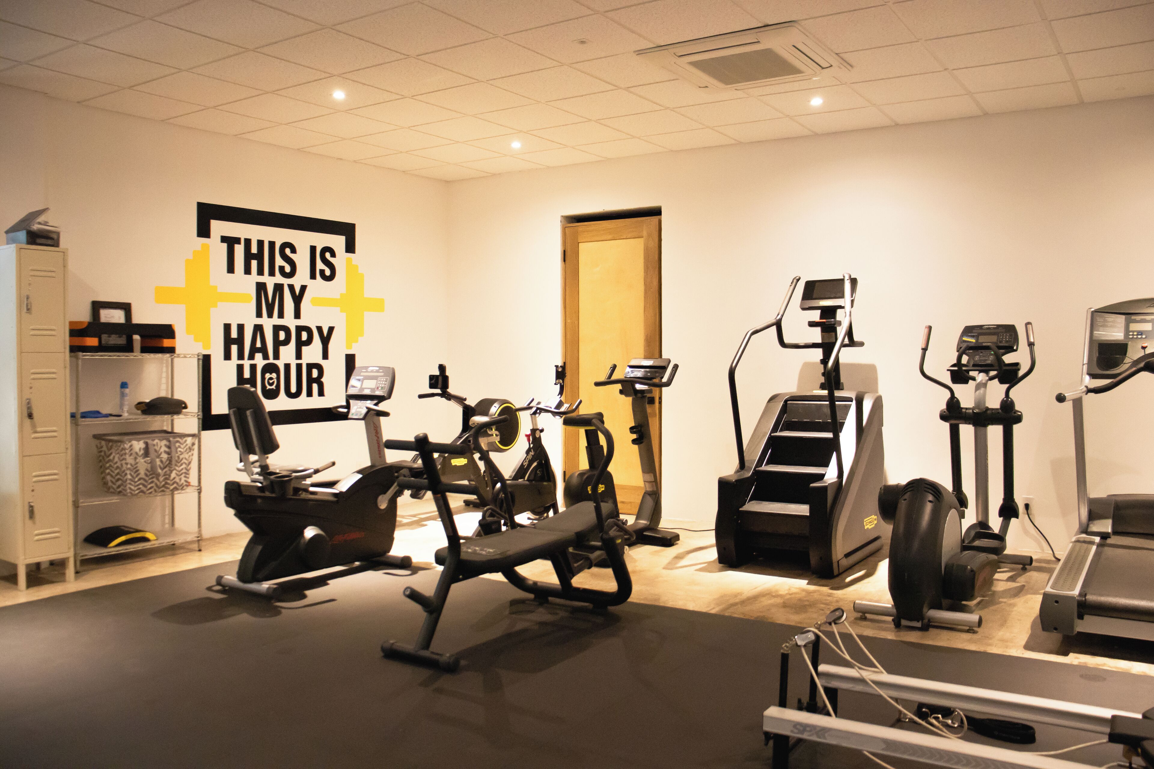 Une salle de sport équipée de divers appareils d’exercice, d’un tapis de course et d’une pancarte sur laquelle on peut lire : « ICI, C’EST LE MOMENT DE LA DÉTENTE ».