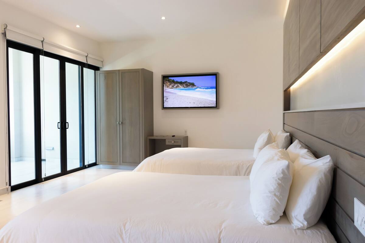 Quarto moderno com uma cama grande, televisão montada na parede e porta de correr de vidro para uma varanda.