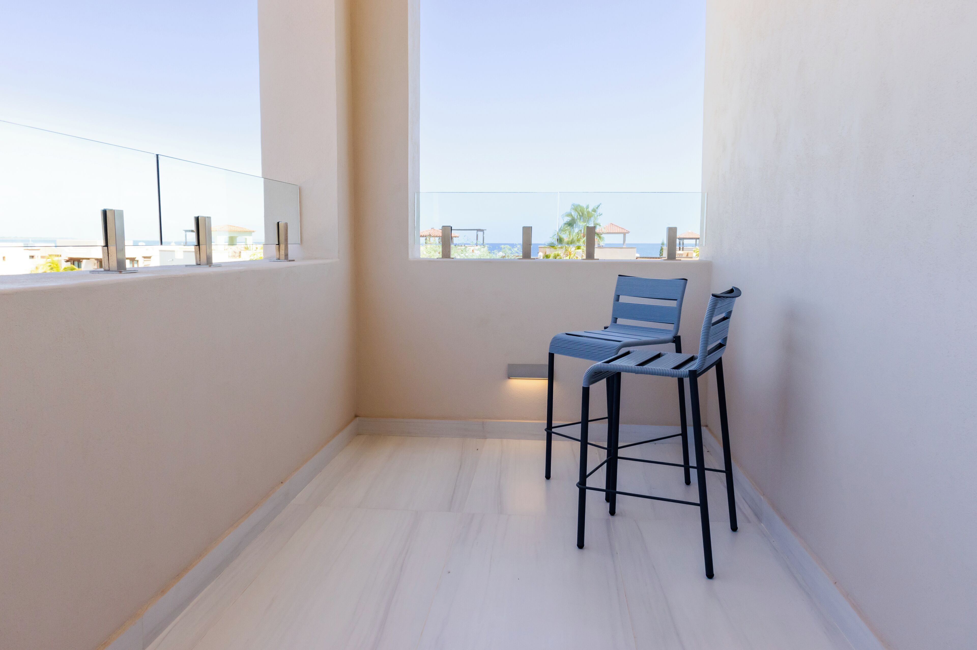 A balcony with a view of the sea, featuring two blue chairs and a small table.