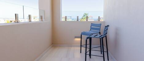 Un balcon avec vue sur la mer, agrémenté de deux chaises bleues et d’une petite table.