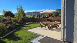 Un patio con mesa y sillas, una sombrilla y vistas a un paisaje verde con colinas y árboles.