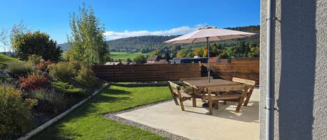 A patio with a table and chairs, an umbrella, and a view of a green landscape with hills and trees.