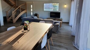 Una sala moderna con una mesa de comedor de madera, un sofá, un televisor y una escalera.