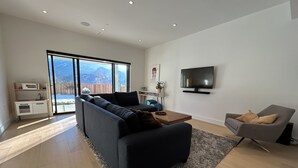 A modern living room with a sofa, a coffee table, a TV, and a chair. - Mountain View Home w/ Gym, Sauna & Cold Plunge (Squamish)