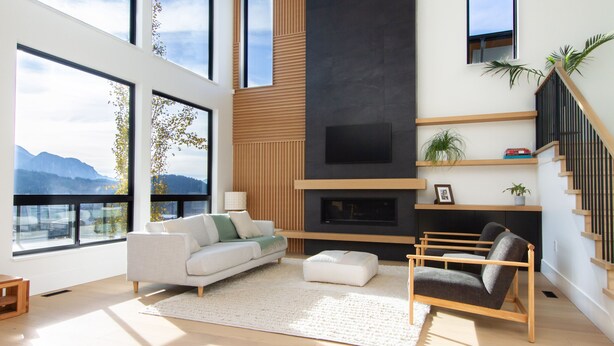 A modern living room with a sofa, ottoman, and a fireplace. - Mountain View Home w/ Gym, Sauna & Cold Plunge (Squamish)